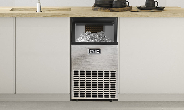 Built-in stainless steel ice maker installed under wooden countertop displaying clear ice cubes in viewing window with digital control panel.