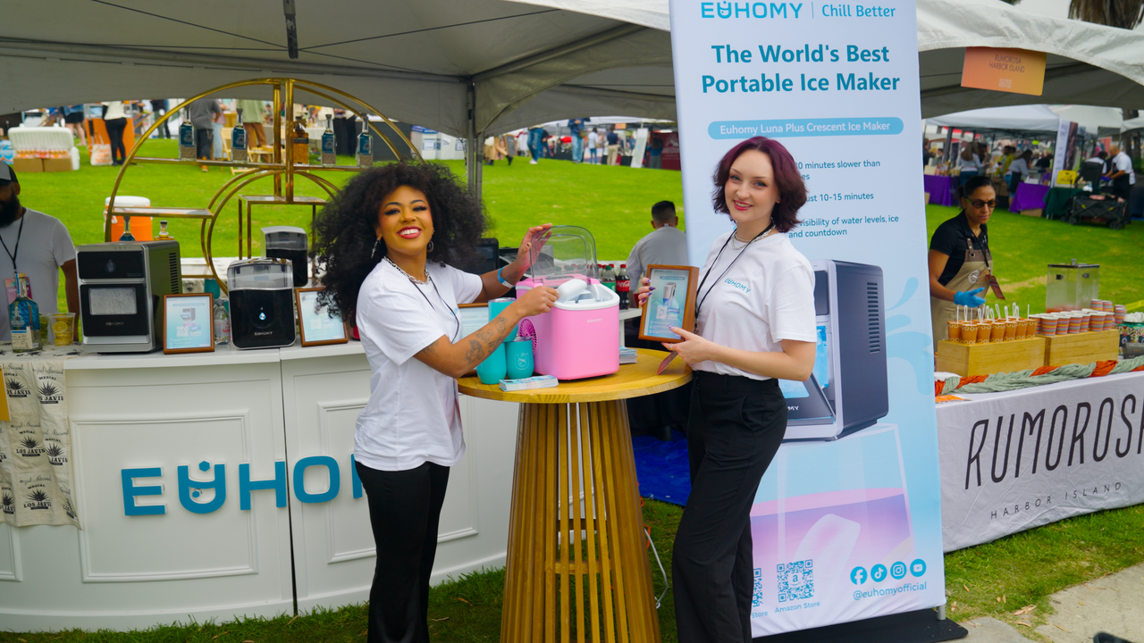 Euhomy brand representatives demonstrating a pink portable ice maker at an outdoor event booth featuring multiple countertop ice maker models.